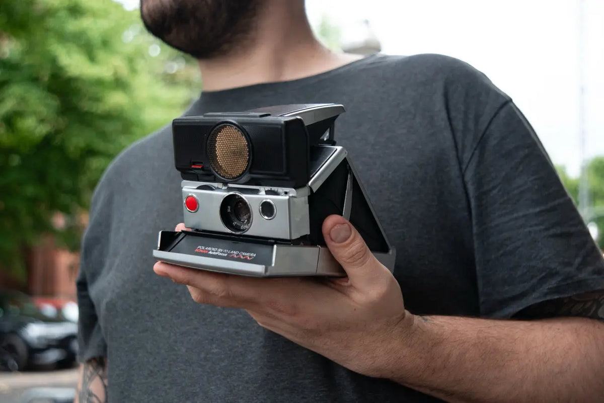 Person holding a folding Polaroid SX-70 camera outdoors