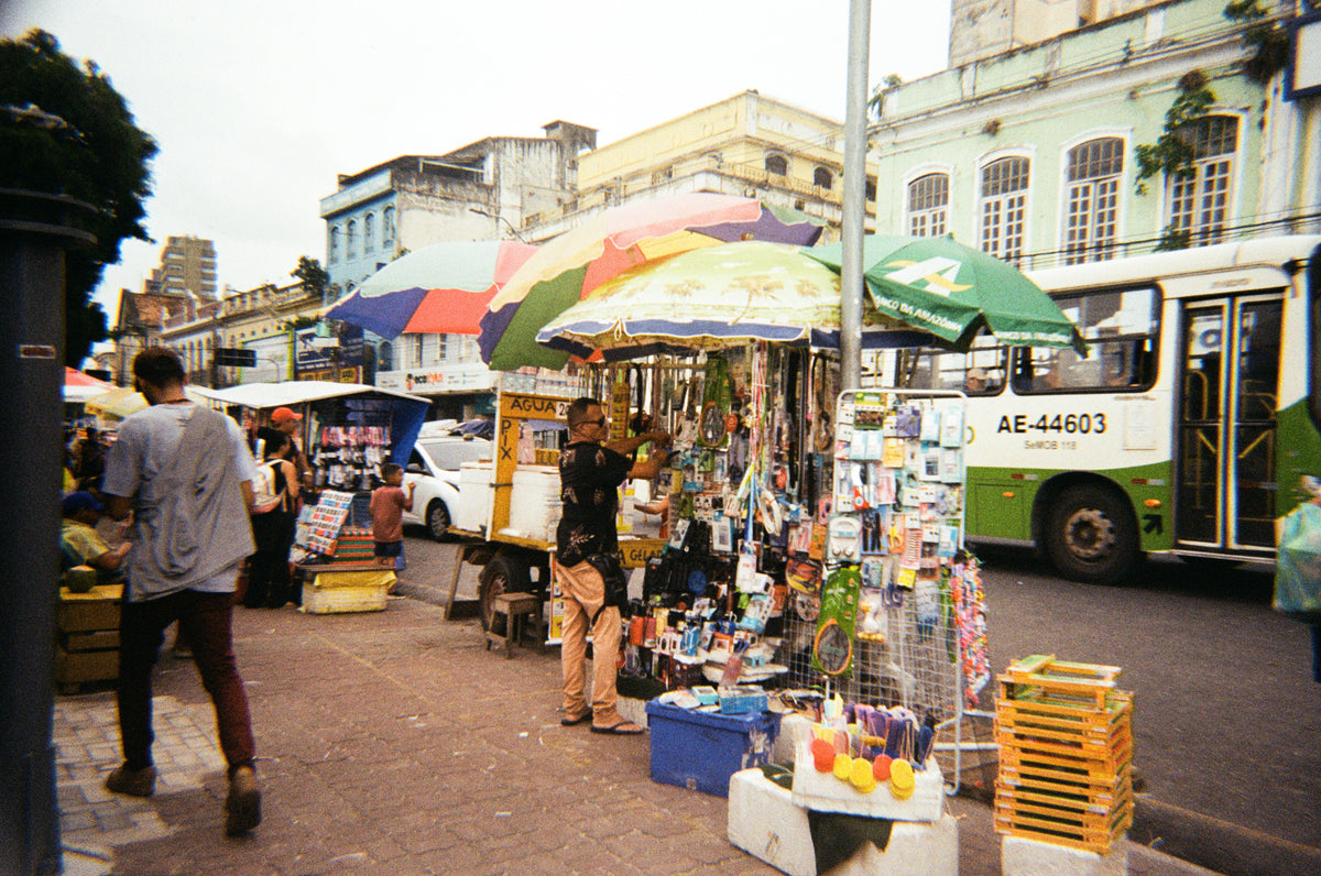 Colourful market umbrellas and stalls line a busy street beside a bus.