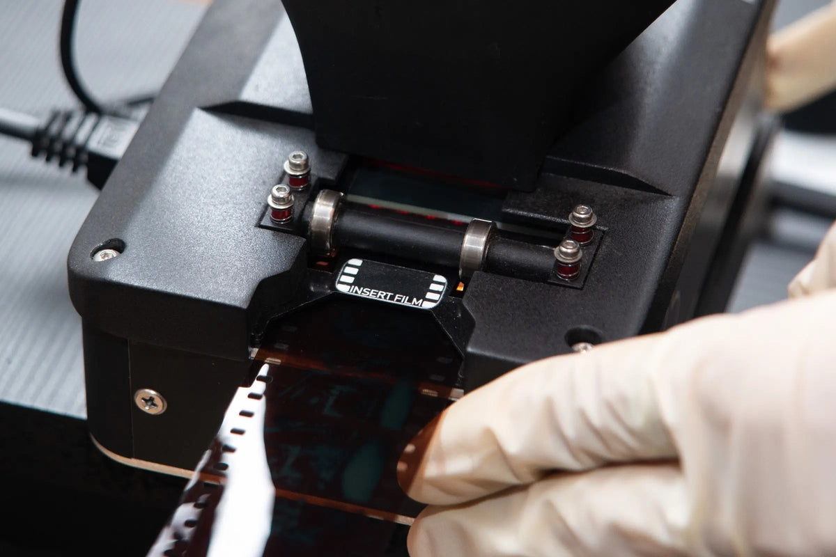 Gloved hands handling film in a camera scanning setup